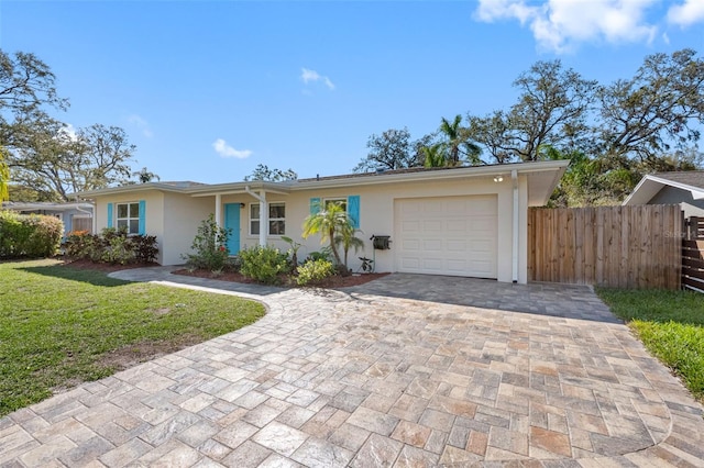 ranch-style home featuring an attached garage, fence, decorative driveway, stucco siding, and a front lawn