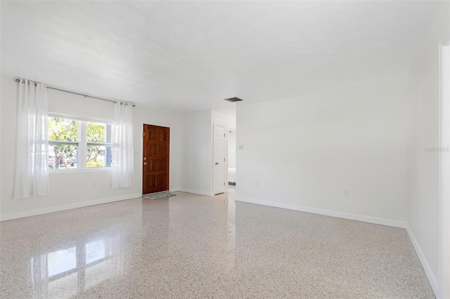 unfurnished room with baseboards, visible vents, and light speckled floor