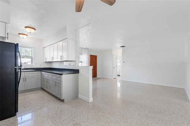 kitchen featuring dark countertops, open floor plan, freestanding refrigerator, light speckled floor, and backsplash