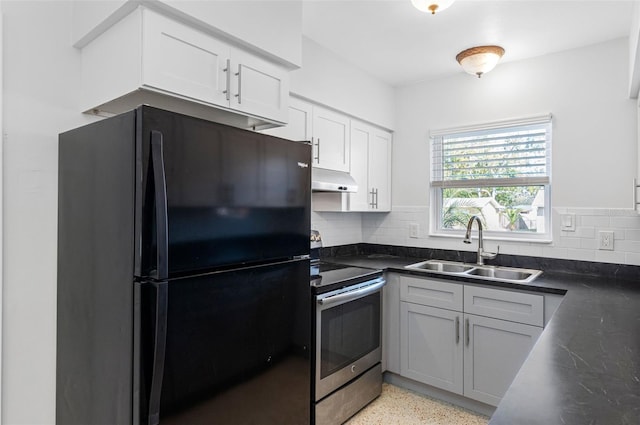 kitchen featuring dark countertops, stainless steel electric range oven, freestanding refrigerator, light speckled floor, and a sink