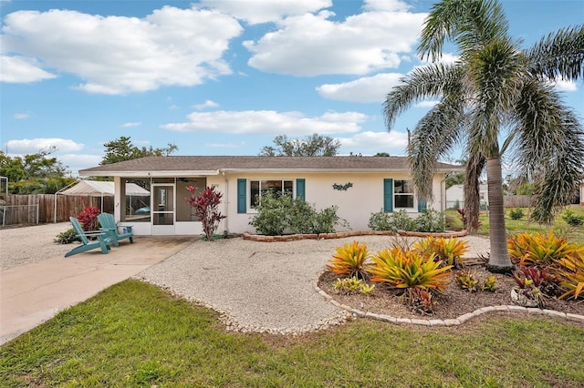 view of front of house with a patio, stucco siding, a front yard, a sunroom, and fence