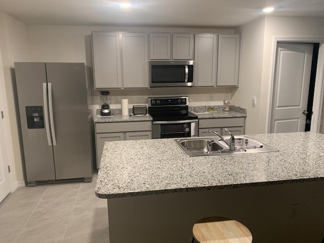 kitchen featuring light stone countertops, appliances with stainless steel finishes, gray cabinets, and a sink