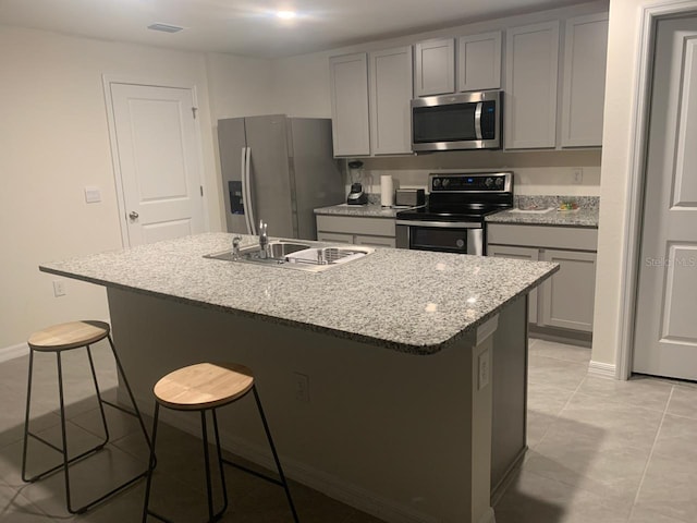 kitchen with an island with sink, light stone countertops, appliances with stainless steel finishes, and a breakfast bar area