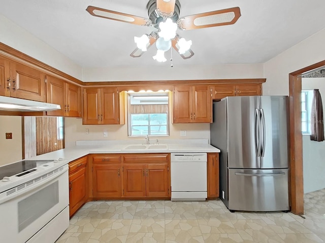 kitchen featuring under cabinet range hood, white appliances, a sink, light countertops, and brown cabinets