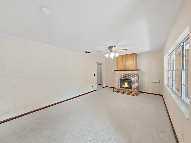 unfurnished living room featuring light colored carpet, a ceiling fan, baseboards, visible vents, and a brick fireplace