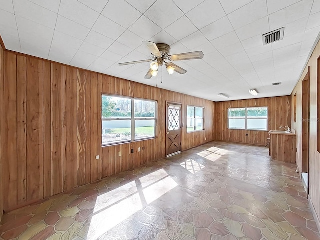 empty room with wood walls, ceiling fan, and visible vents