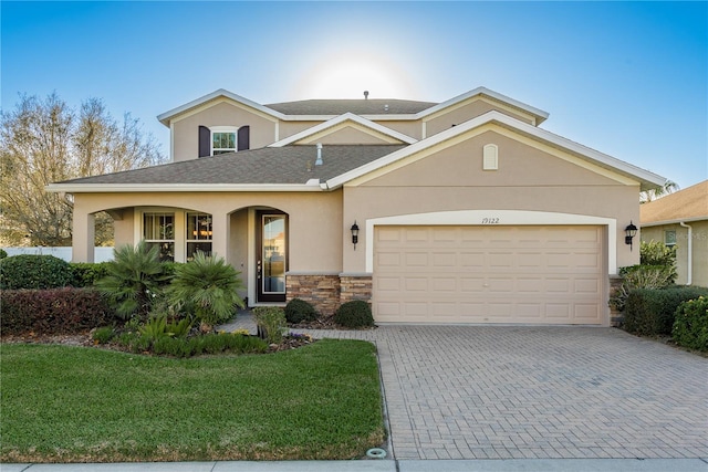 view of front of property featuring decorative driveway, stucco siding, a garage, stone siding, and a front lawn