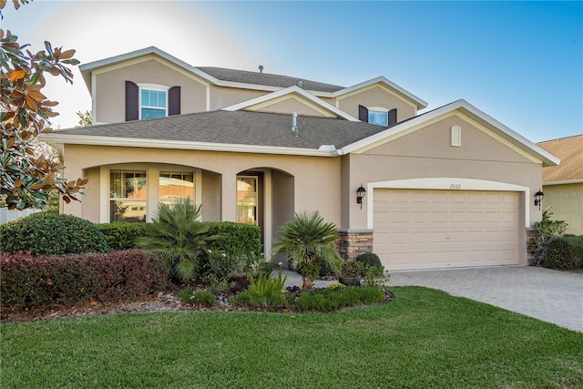 view of front facade featuring an attached garage, a shingled roof, a front yard, and stucco siding