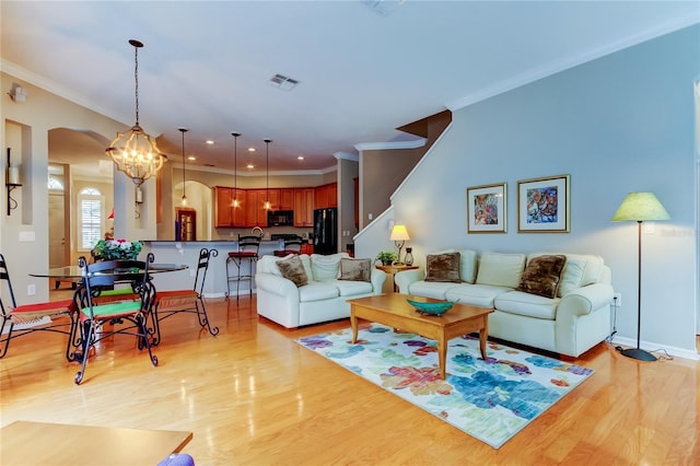 living room with light wood finished floors, visible vents, arched walkways, and ornamental molding