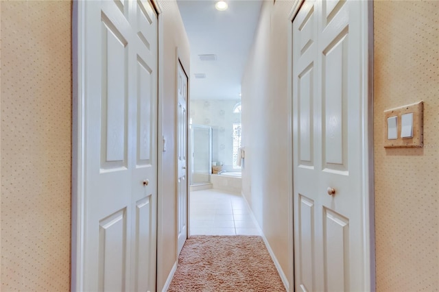 corridor featuring wallpapered walls, light tile patterned floors, and light colored carpet