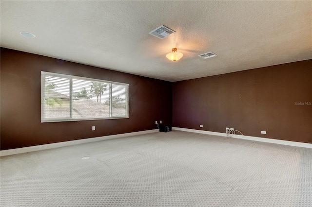 empty room featuring light carpet, a textured ceiling, visible vents, and baseboards