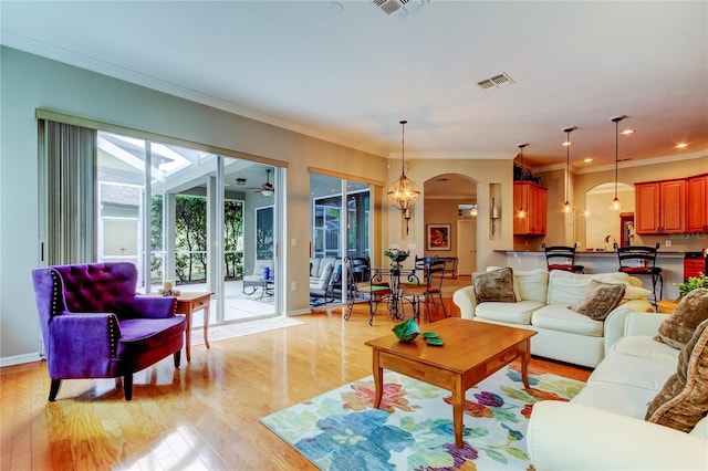 living room featuring arched walkways, light wood finished floors, ornamental molding, and visible vents