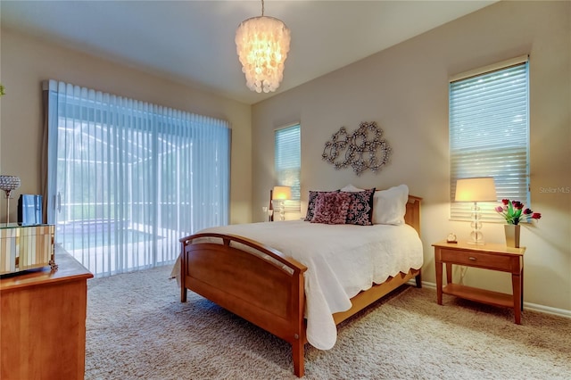 carpeted bedroom with a notable chandelier, multiple windows, baseboards, and access to exterior