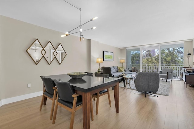 dining space with light wood-style flooring, expansive windows, a chandelier, and baseboards