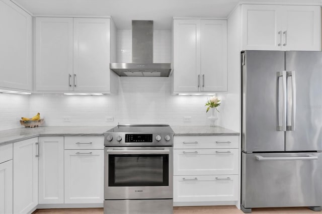 kitchen featuring stainless steel appliances, white cabinetry, light stone counters, and wall chimney exhaust hood