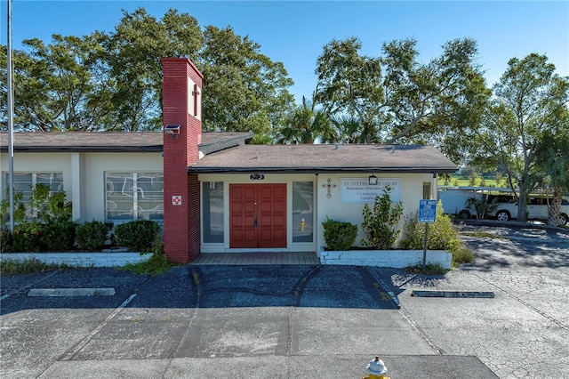 view of front of property featuring uncovered parking, a chimney, and stucco siding