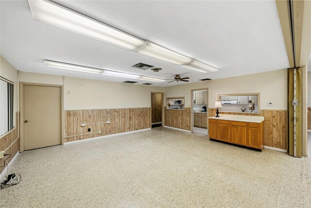 unfurnished room with a wainscoted wall, wood walls, visible vents, and ceiling fan