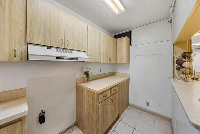 kitchen with under cabinet range hood, light tile patterned floors, light countertops, and light brown cabinetry