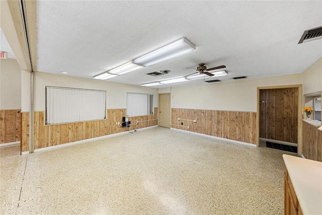 empty room featuring wooden walls, a wainscoted wall, and a textured ceiling