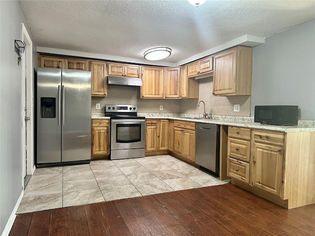 kitchen featuring light wood finished floors, tasteful backsplash, appliances with stainless steel finishes, under cabinet range hood, and a sink