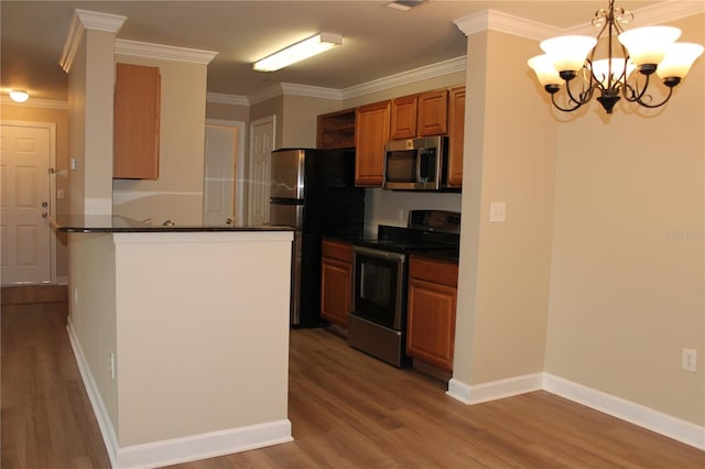 kitchen with stainless steel appliances, a peninsula, brown cabinetry, dark countertops, and decorative light fixtures