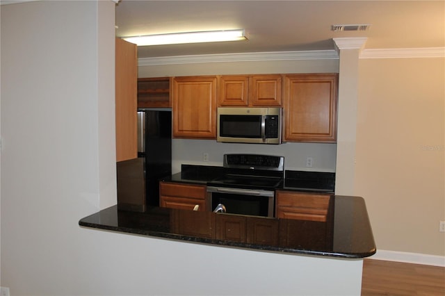 kitchen with dark stone counters, ornamental molding, brown cabinets, a peninsula, and stainless steel appliances