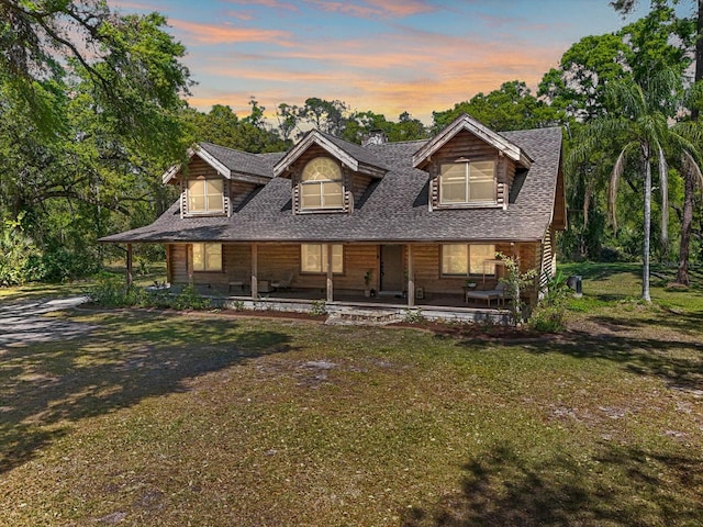 view of front of house with a shingled roof and a yard