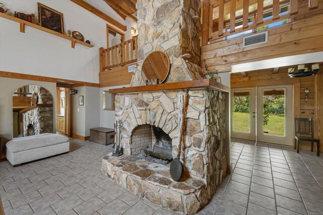 tiled living area featuring beam ceiling, a stone fireplace, a high ceiling, and visible vents