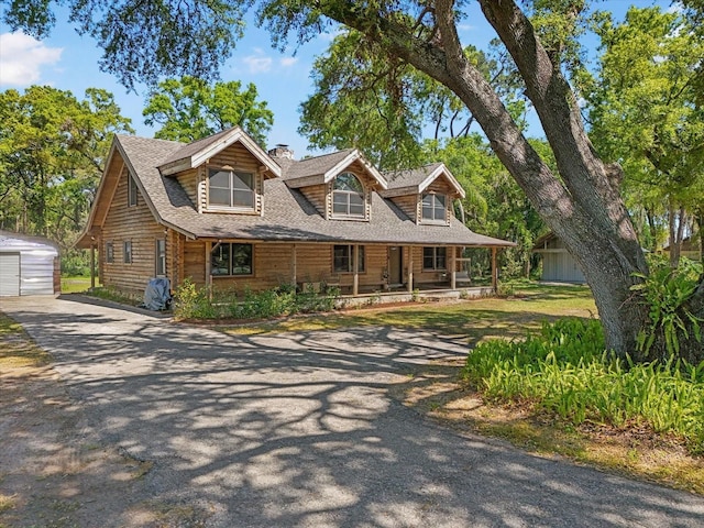 view of front of house featuring aphalt driveway, roof with shingles, covered porch, a garage, and an outbuilding