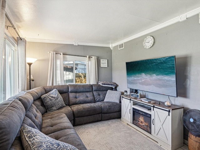 living area featuring visible vents, a glass covered fireplace, crown molding, and light colored carpet