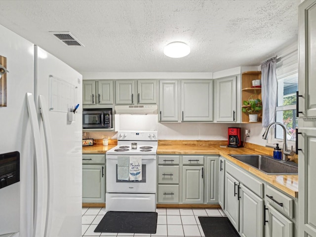 kitchen with light tile patterned floors, under cabinet range hood, white appliances, a sink, and visible vents