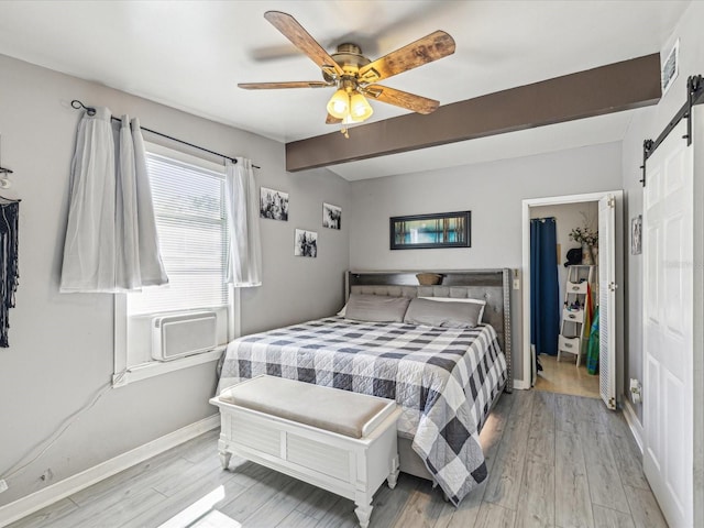 bedroom featuring light wood-style floors, visible vents, beamed ceiling, and a barn door