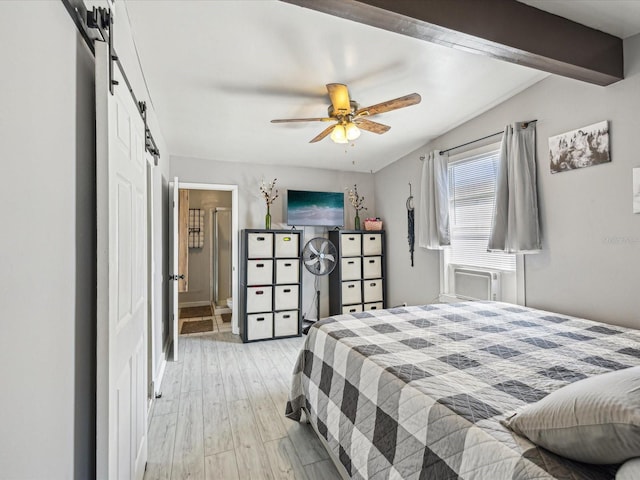 bedroom featuring a barn door, light wood-style flooring, a ceiling fan, beam ceiling, and ensuite bath