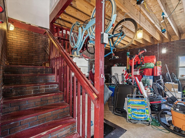 stairway featuring brick wall, concrete floors, and beamed ceiling