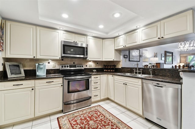 kitchen with a tray ceiling, light tile patterned floors, stainless steel appliances, recessed lighting, and a sink