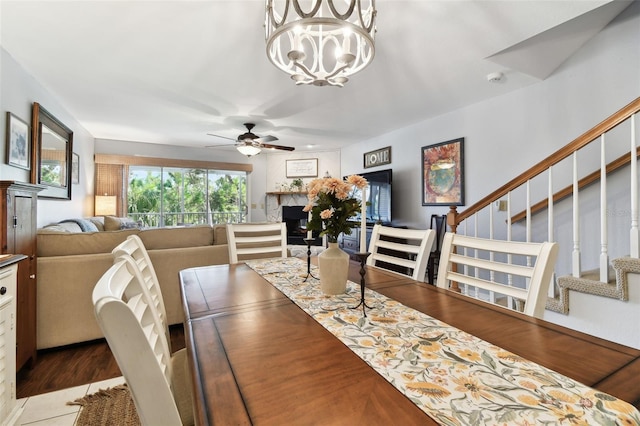 dining area featuring stairs, a fireplace, and ceiling fan with notable chandelier