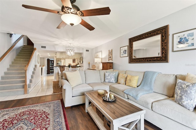 living area with ceiling fan with notable chandelier, visible vents, stairway, and wood finished floors