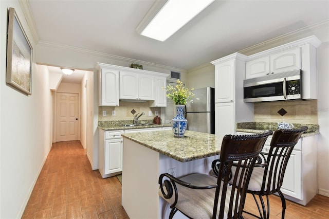 kitchen featuring white cabinets, light stone counters, stainless steel appliances, and a sink