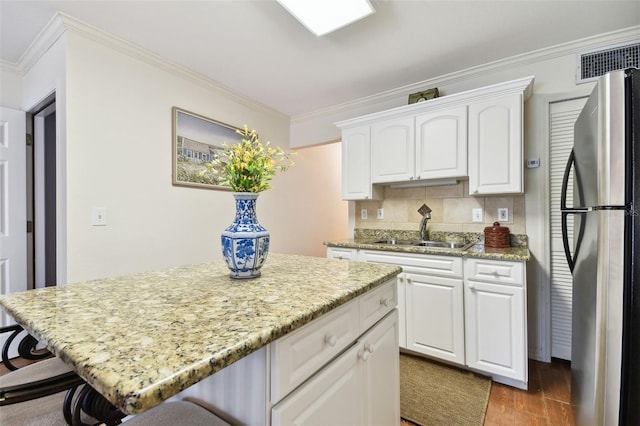 kitchen with freestanding refrigerator, white cabinets, a sink, and a breakfast bar area