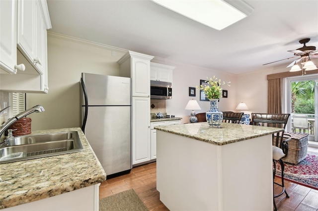 kitchen with a breakfast bar, appliances with stainless steel finishes, wood tiled floor, white cabinetry, and a sink