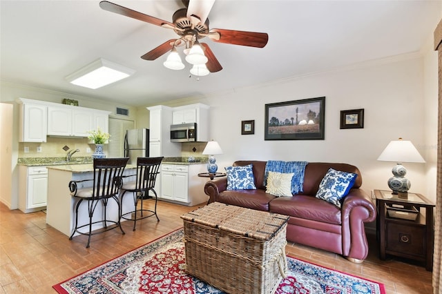 living room featuring a ceiling fan, visible vents, crown molding, and light wood finished floors