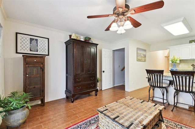 sitting room featuring ceiling fan, ornamental molding, light wood-style flooring, and baseboards