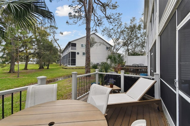 deck with a sunroom, outdoor dining area, and a yard