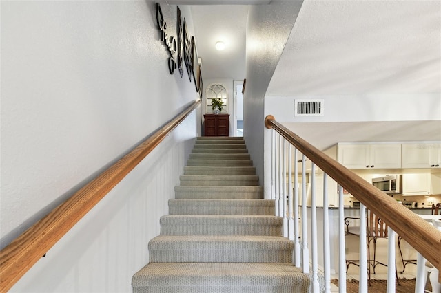 stairs featuring wainscoting, visible vents, and a textured ceiling