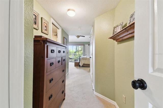 hallway with light carpet, a textured wall, a textured ceiling, and baseboards