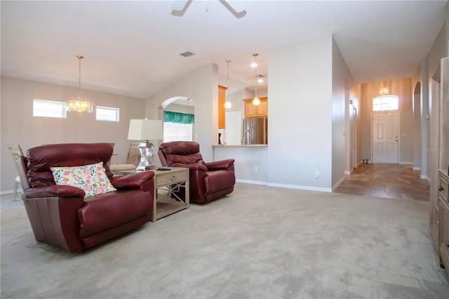 living room featuring visible vents, baseboards, lofted ceiling, ceiling fan with notable chandelier, and light colored carpet