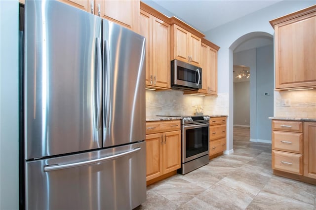 kitchen with light stone counters, arched walkways, light brown cabinetry, appliances with stainless steel finishes, and backsplash