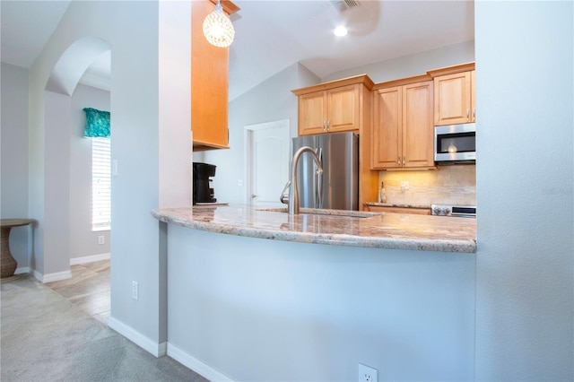 kitchen featuring light stone counters, baseboards, a peninsula, arched walkways, and appliances with stainless steel finishes