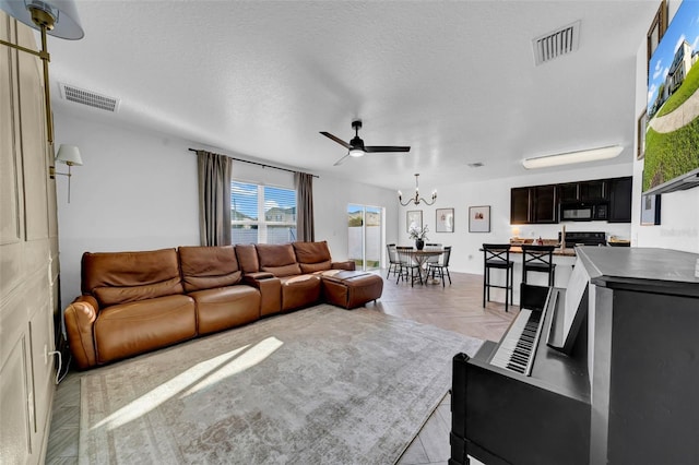 living room featuring visible vents, a textured ceiling, and ceiling fan with notable chandelier