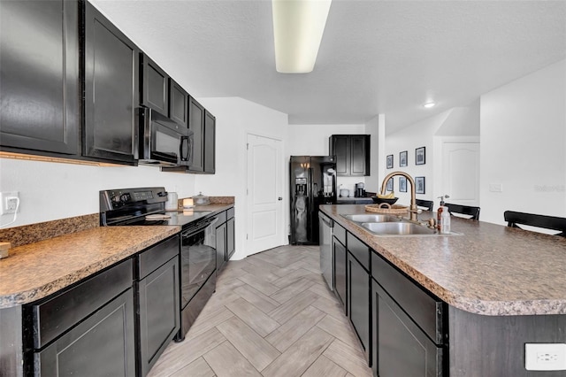 kitchen featuring a kitchen island with sink, a sink, a textured ceiling, dark cabinets, and black appliances